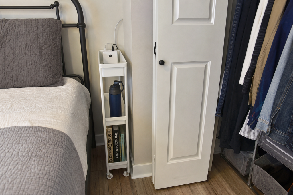 A 7-inch-wide white rolling utility cart tucked into a narrow gap between a bed frame and a closet wall
